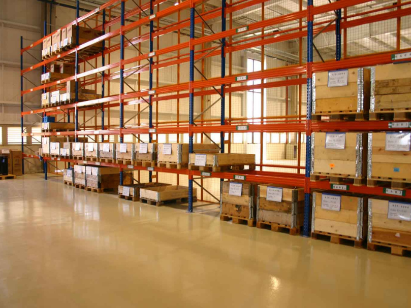 Armazém com piso epóxi bege e estantes metálicas altas contendo caixas de madeira sobre pallets.