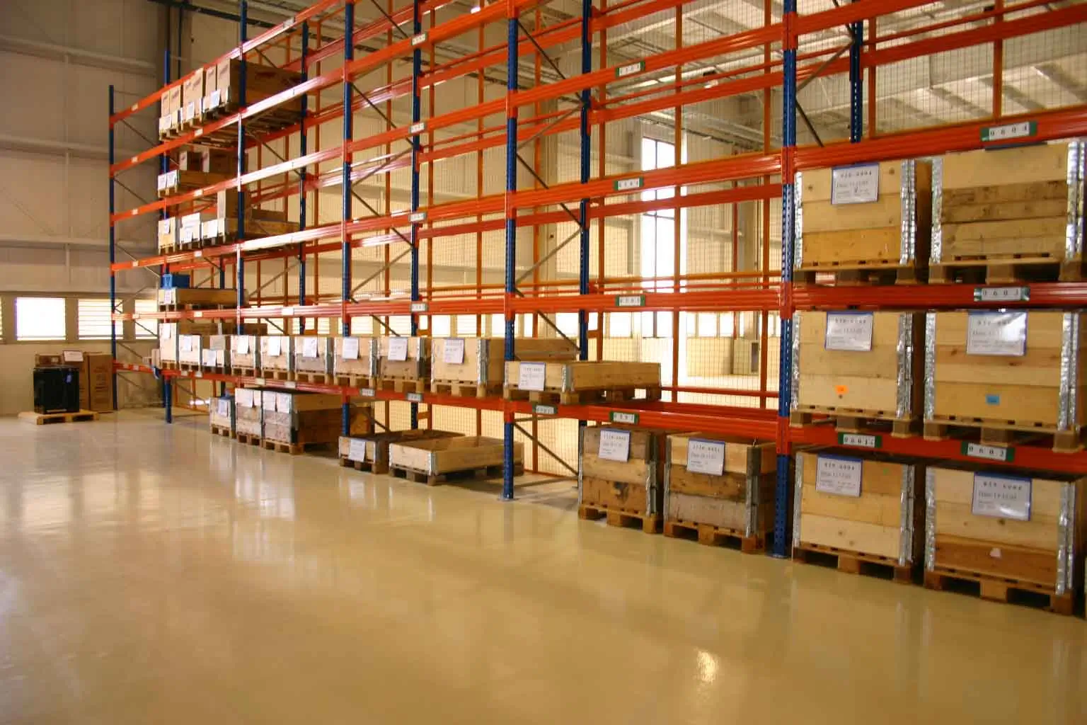 Galpão industrial amplo com piso resinado claro recém-instalado, iluminação superior e estruturas metálicas ao fundo.