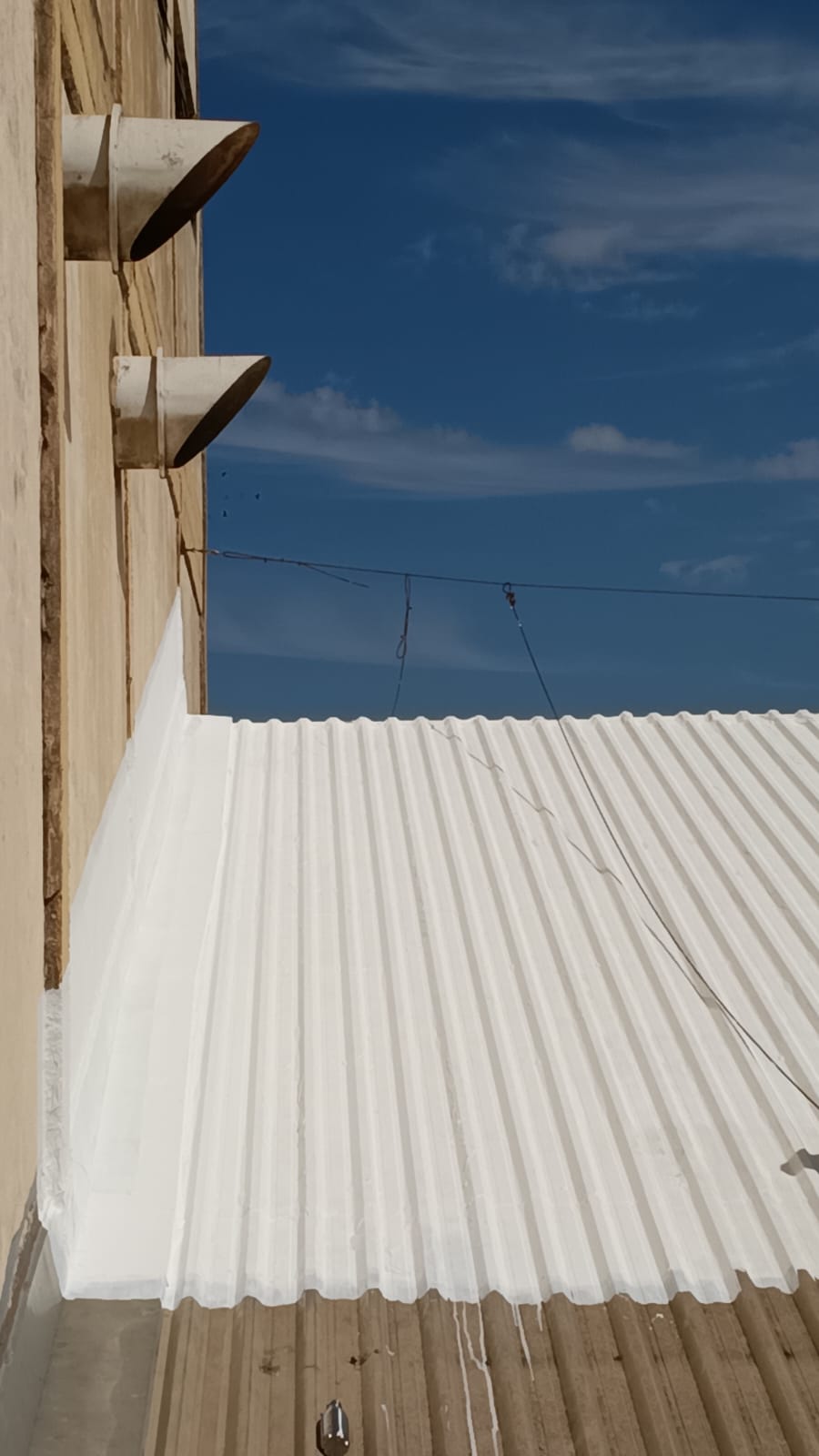 Detalhe do telhado corrugado impermeabilizado, acabamento branco contínuo sobre a chapa metálica.
