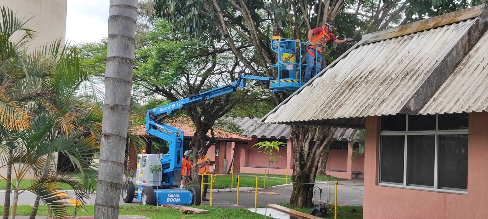 Equipe em plataforma elevatória realizando limpeza de telhado de fibrocimento sujo e desgastado.