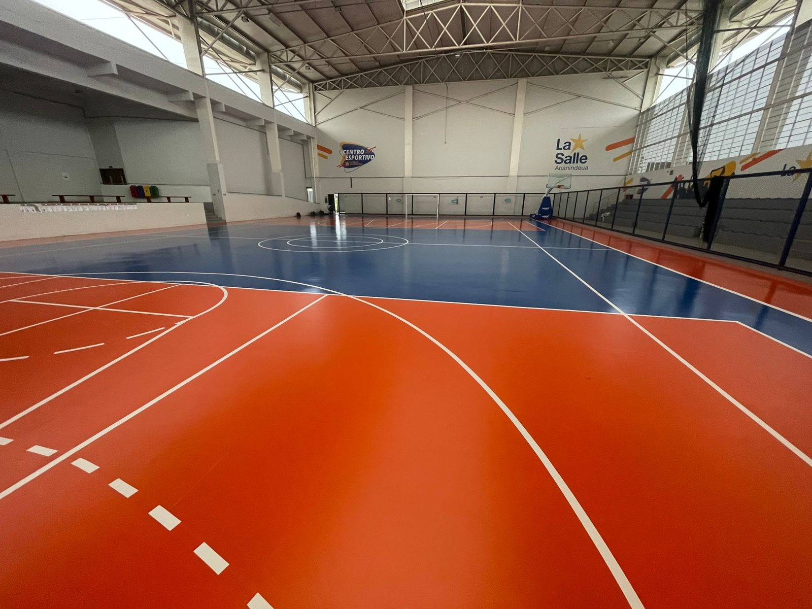Quadra poliesportiva coberta com pintura em azul e laranja, demarcações de basquete e futsal.