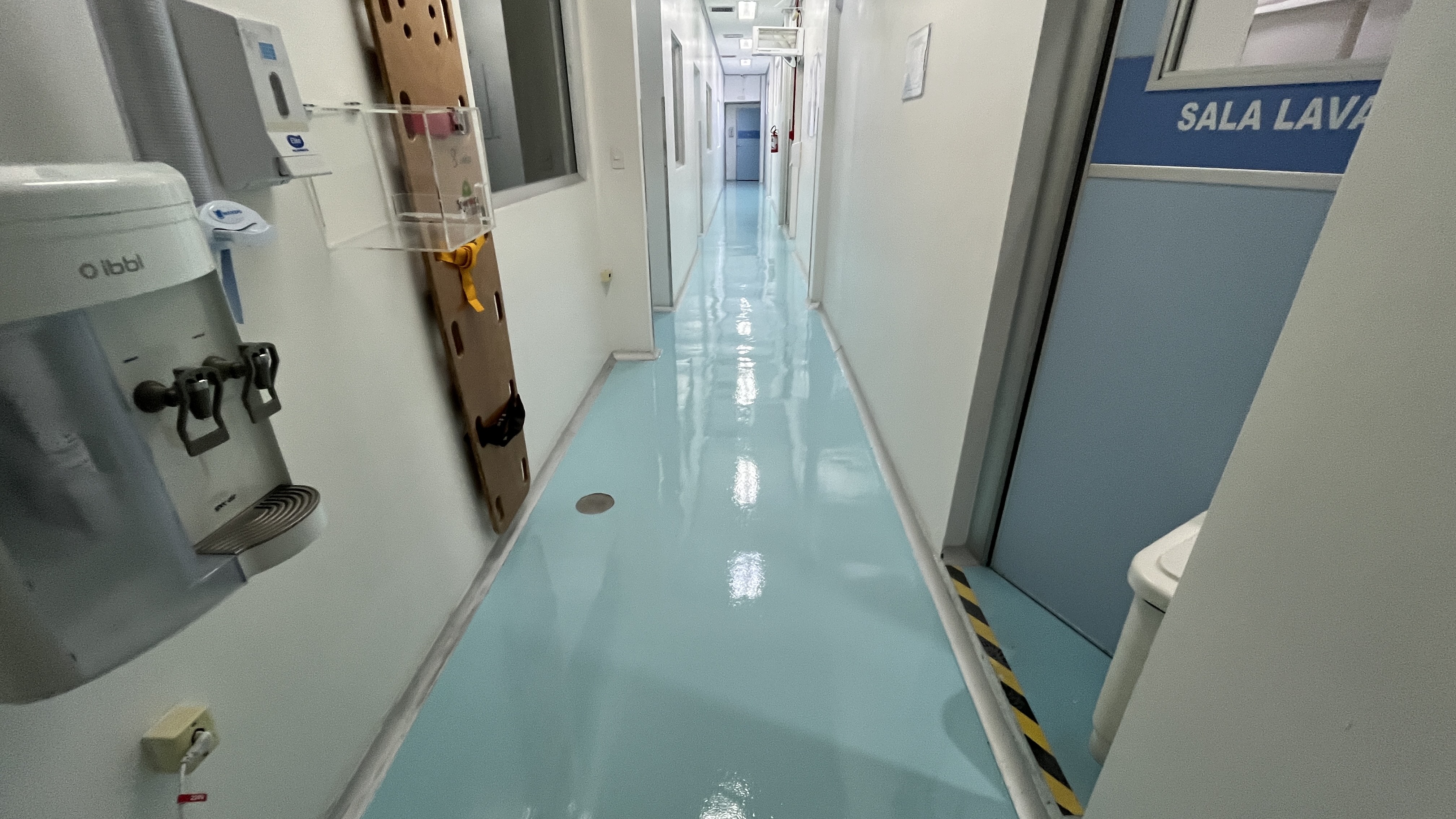 Piso autonivelante contínuo aplicado em corredor de unidade de saúde, sem emendas visíveis e com acabamento espelhado.