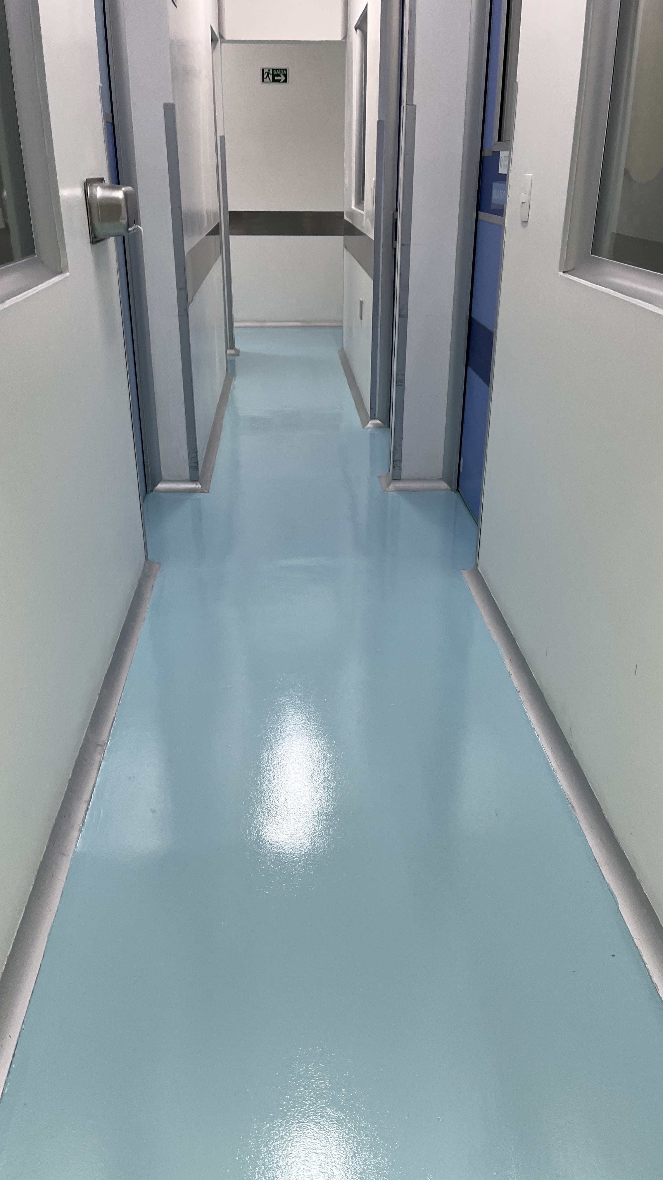 Corredor de laboratório com piso autonivelante verde-água, ideal para ambientes que exigem assepsia e alta resistência química.