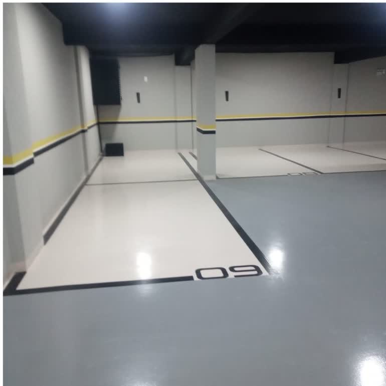 Garagem de condomínio em Curitiba - PR com piso epóxi cinza e branco, vaga demarcada com número e faixa amarela de sinalização.