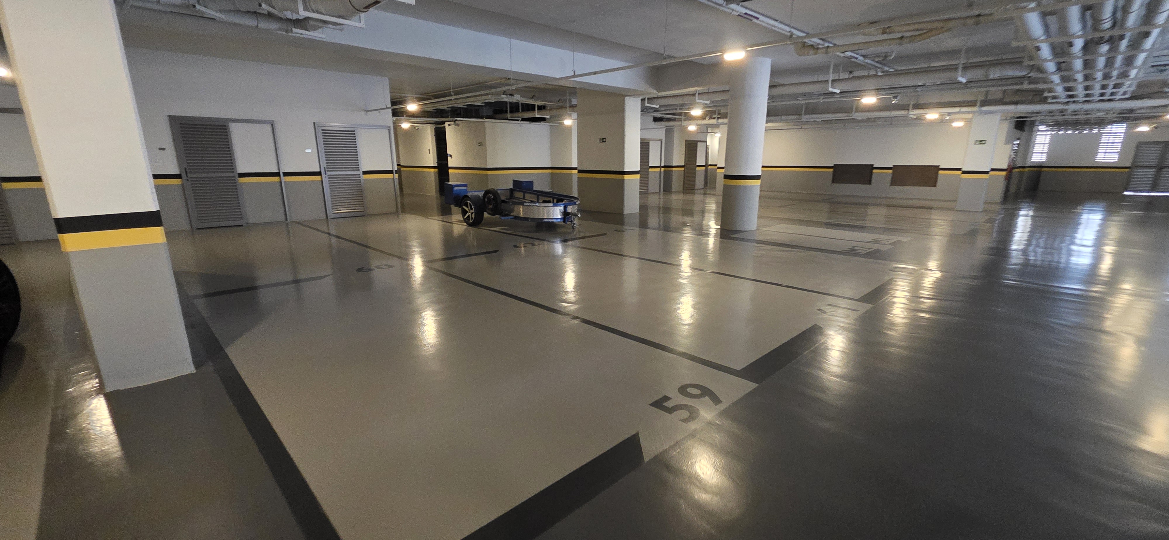 Estacionamento subterrâneo com piso epóxi cinza e seta de circulação branca pintada no chão.