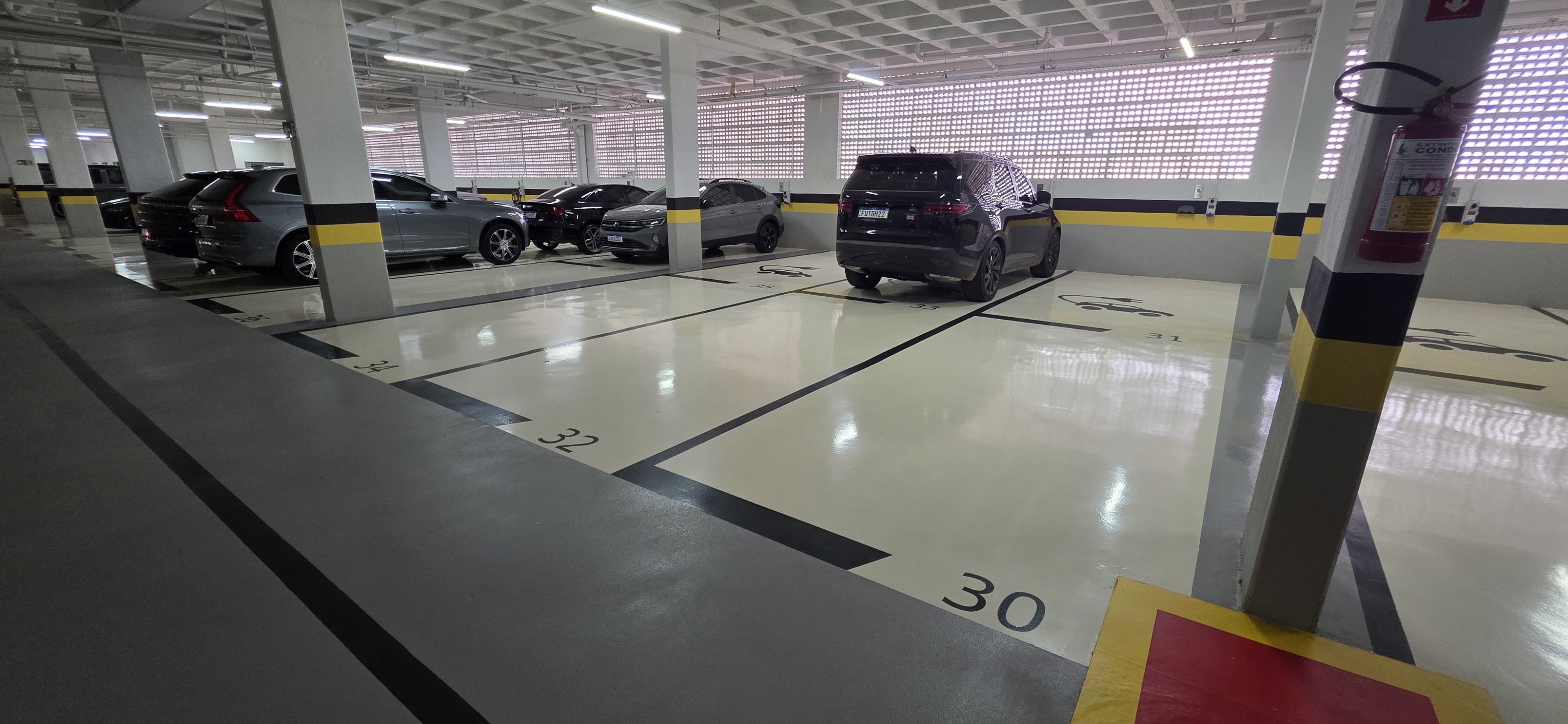 Vagas de garagem demarcadas sobre piso epóxi claro, colunas com faixas de sinalização amarela e preta.