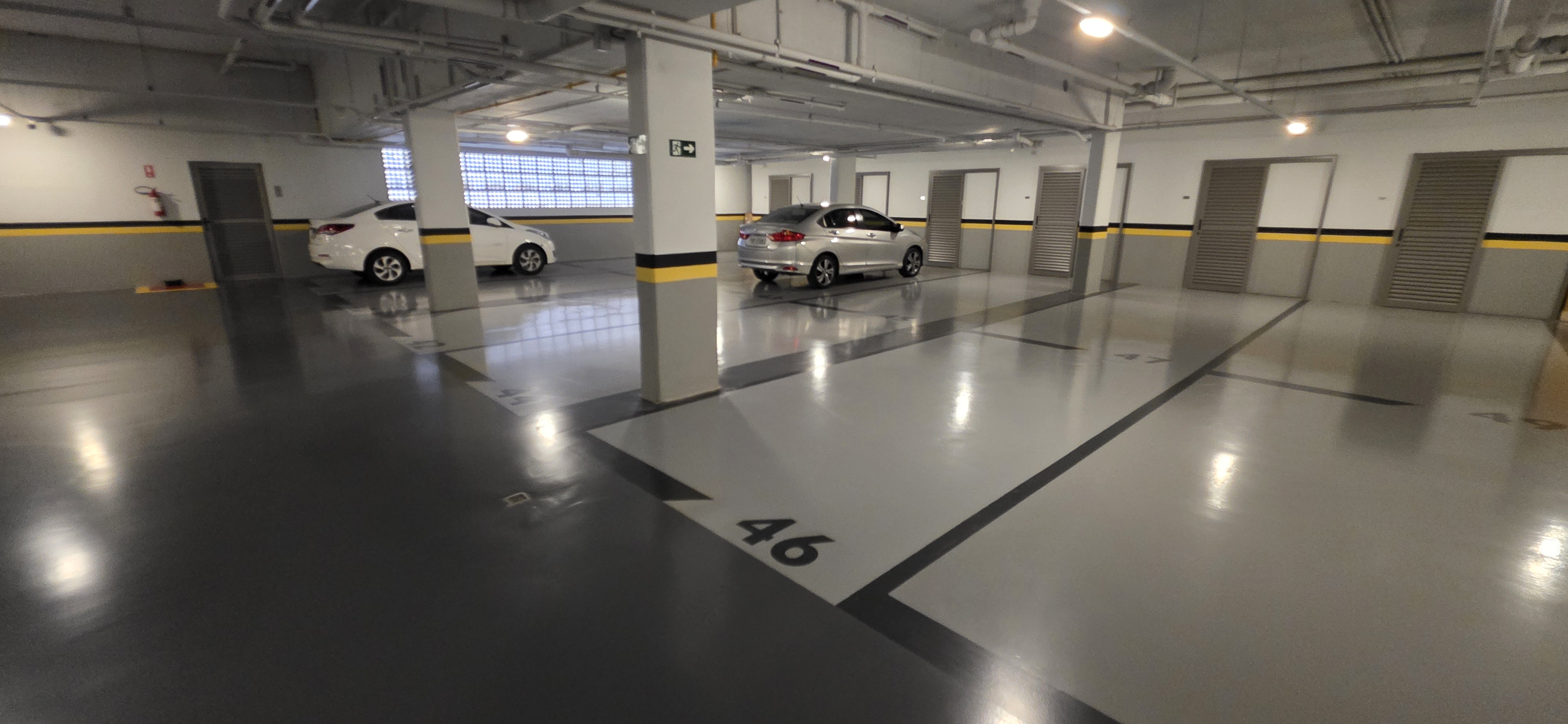 Área de estacionamento com piso epóxi cinza concluído, vagas numeradas e boa refletância de luz.