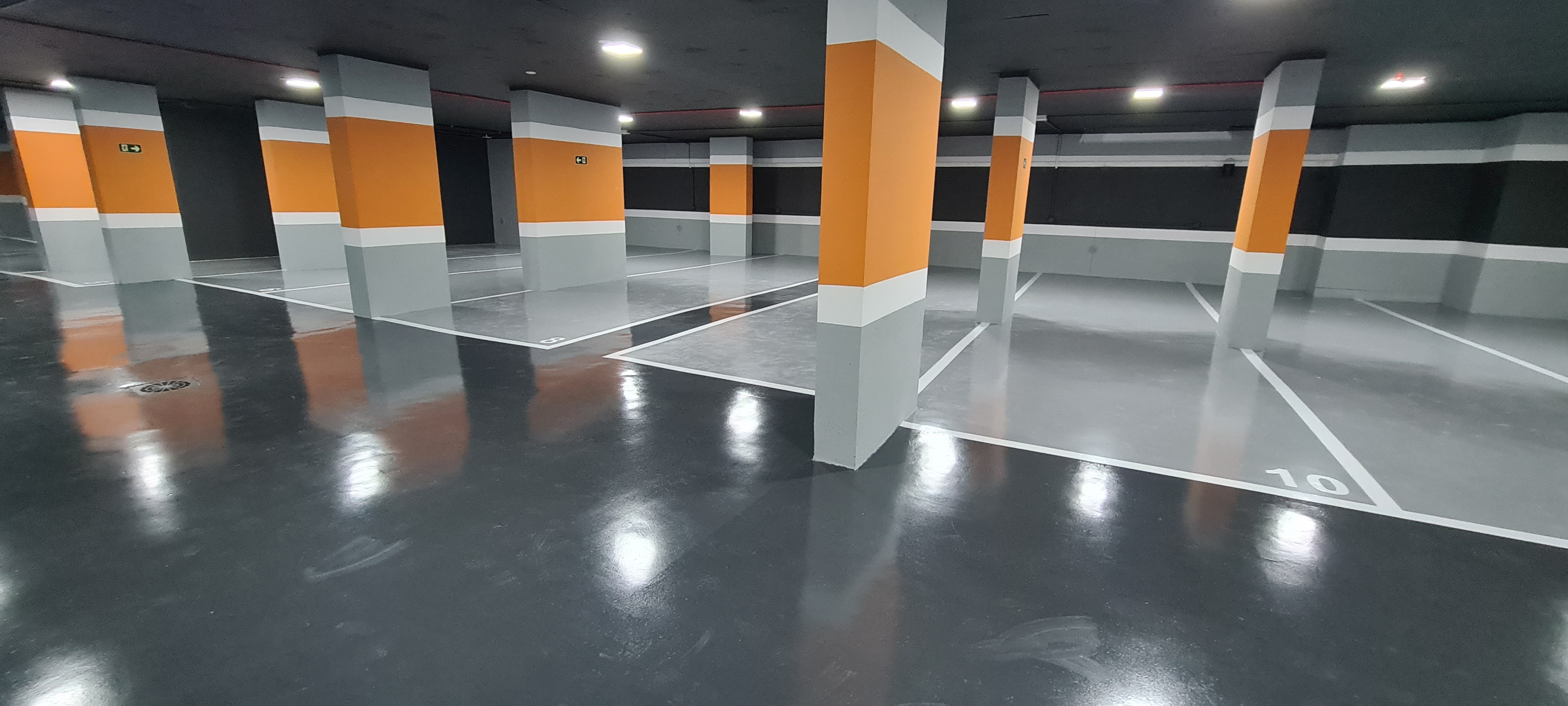 Estacionamento com vagas numeradas e piso epóxi bege e cinza, com várias colunas estruturais.