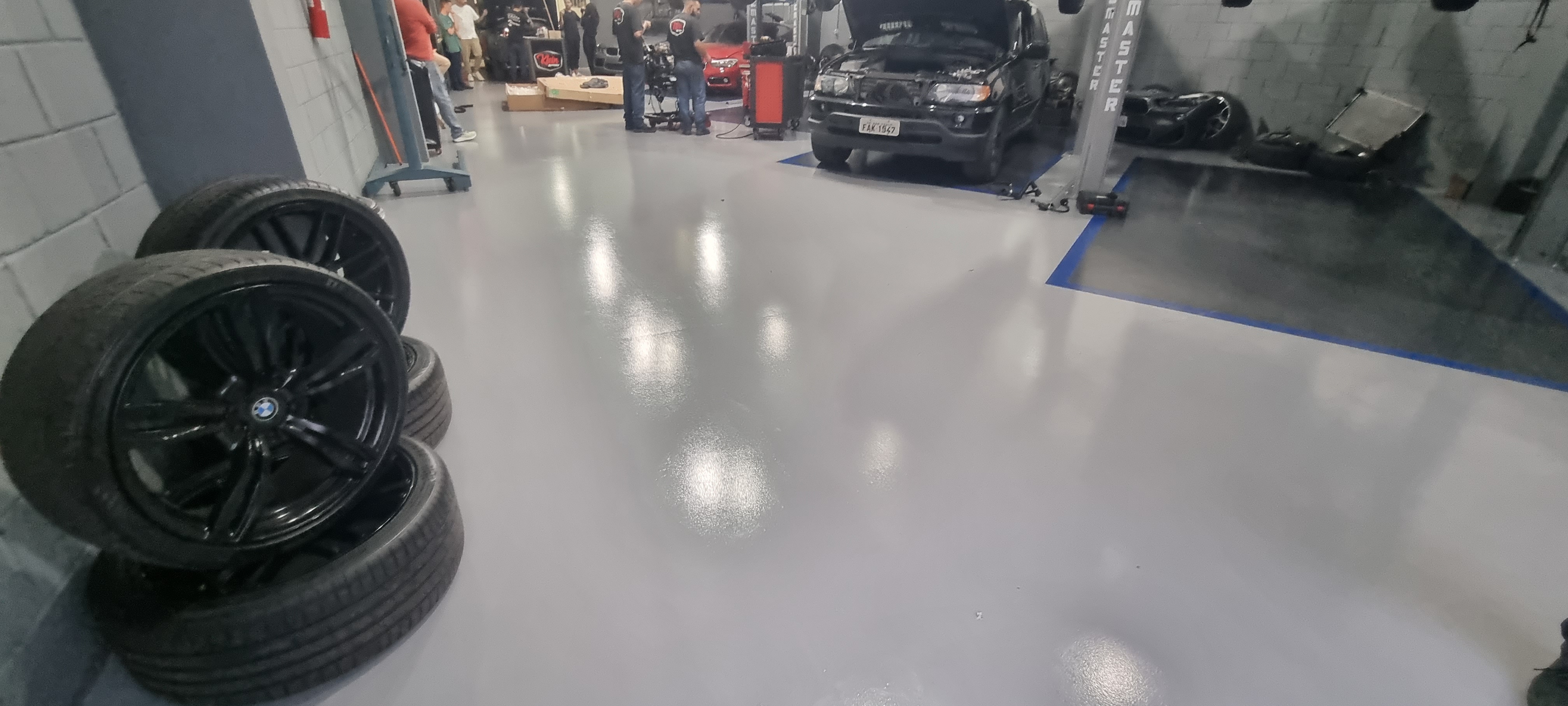 Box de manutenção automotiva com piso epóxi cinza brilhante e veículo elevado para reparo.