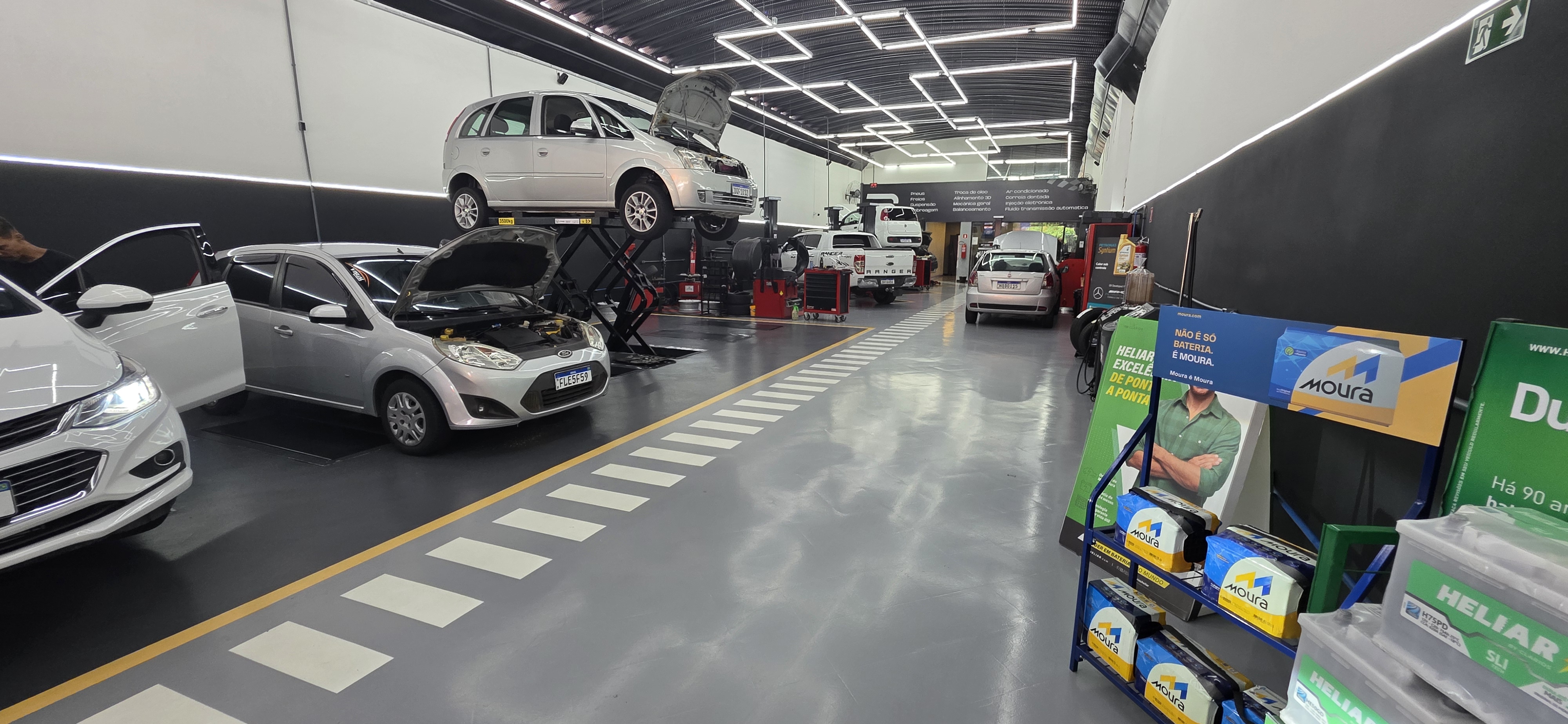 Setor técnico de oficina com piso epóxi cinza, ferramentas e equipamentos organizados junto às baias.