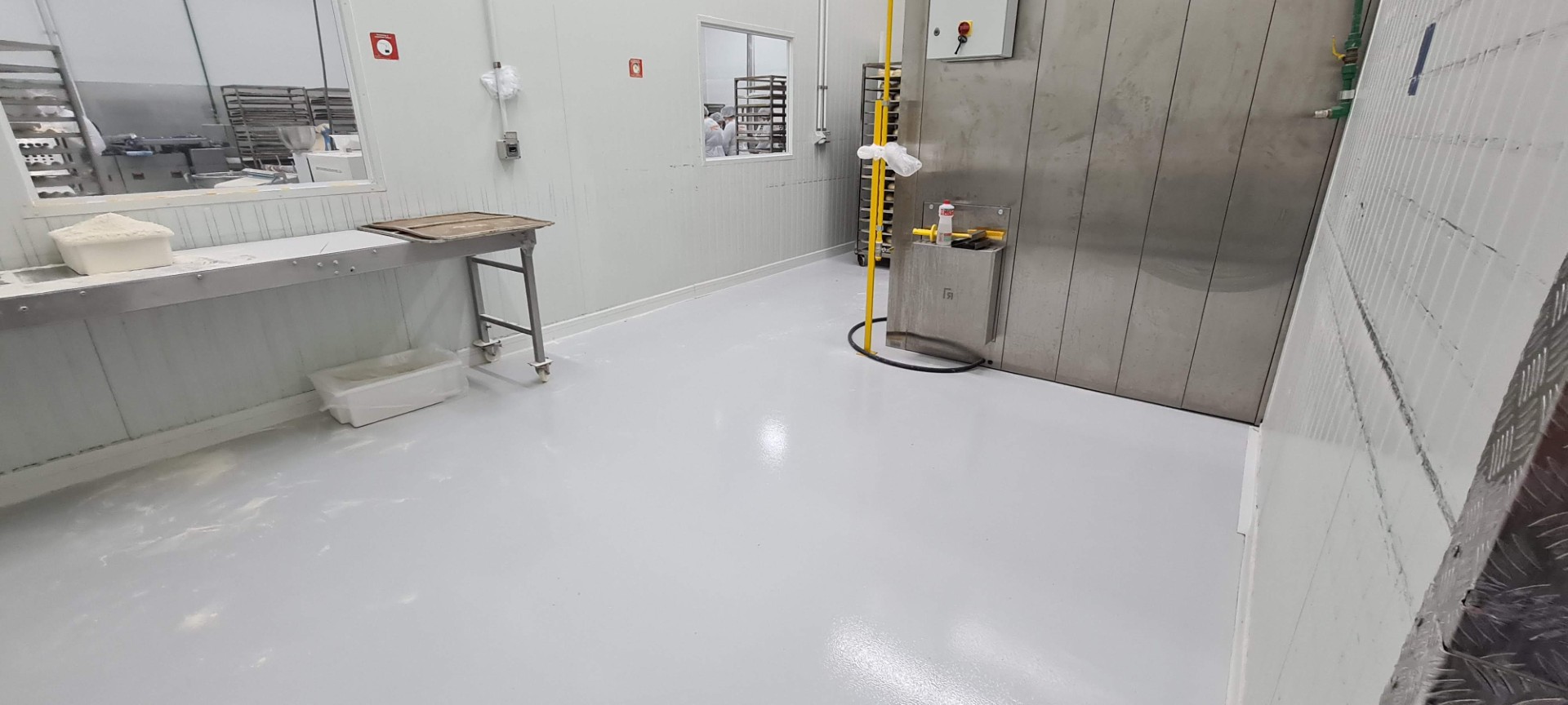 Área interna de indústria alimentícia com piso epóxi cinza claro brilhante e equipamentos inox.
