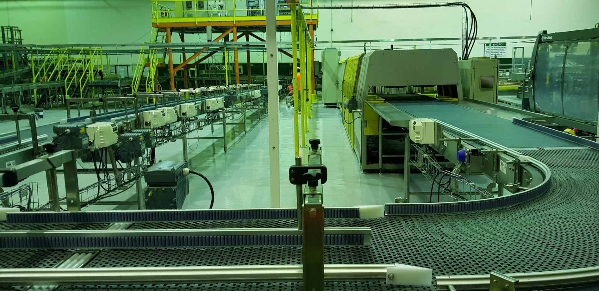 Vista da linha de produção com piso industrial renovado, máquinas automáticas e estruturas metálicas em funcionamento.