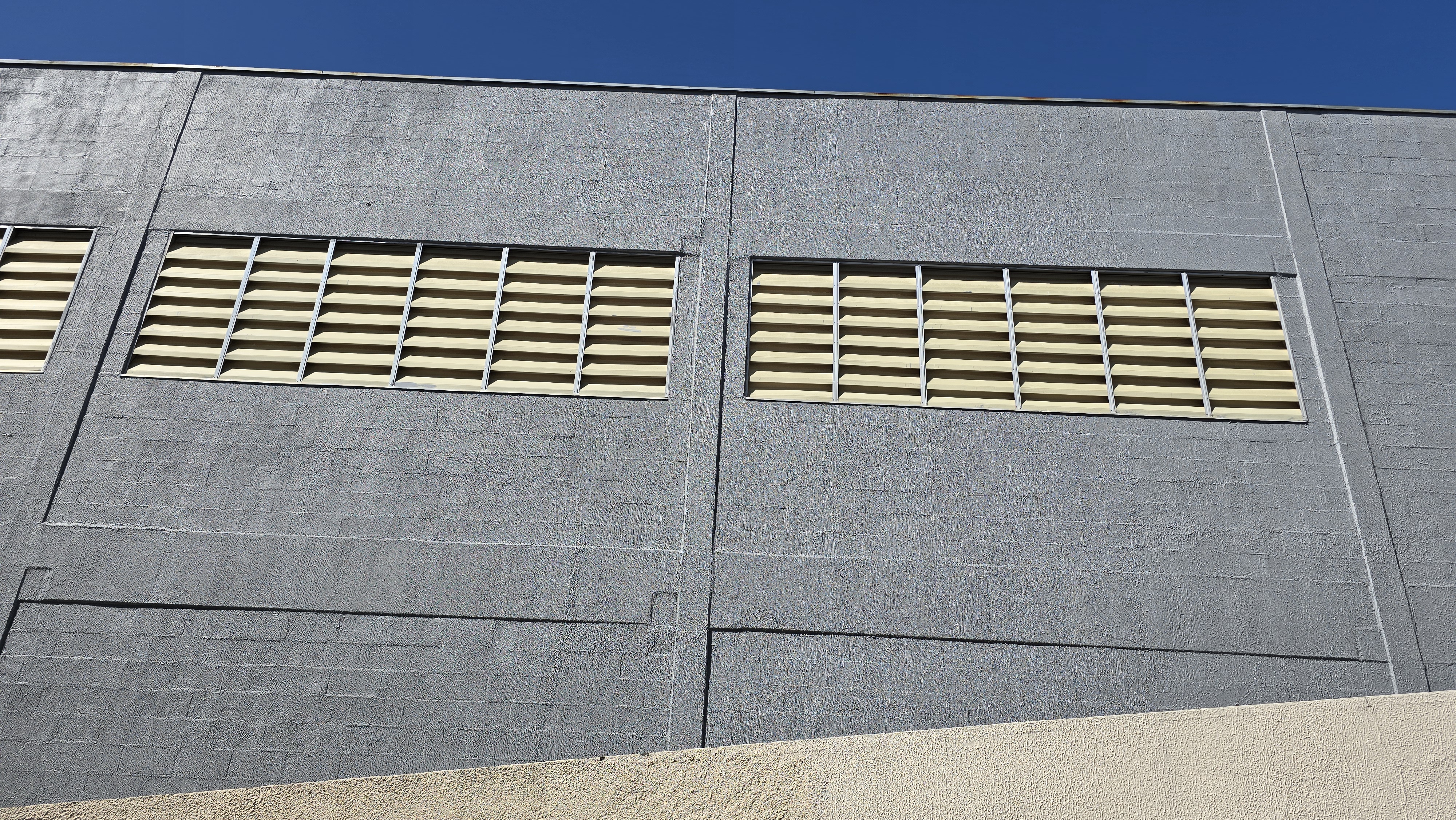 Fachada de galpão industrial pintada com tinta acrílica cinza, aberturas de ventilação em amarelo.