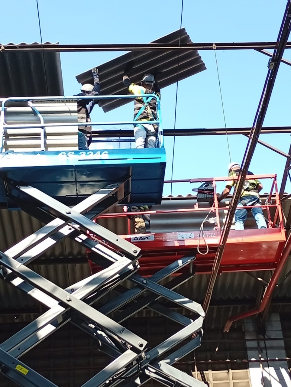 Equipe em plataformas elevatórias substituindo telhas onduladas de cobertura industrial.