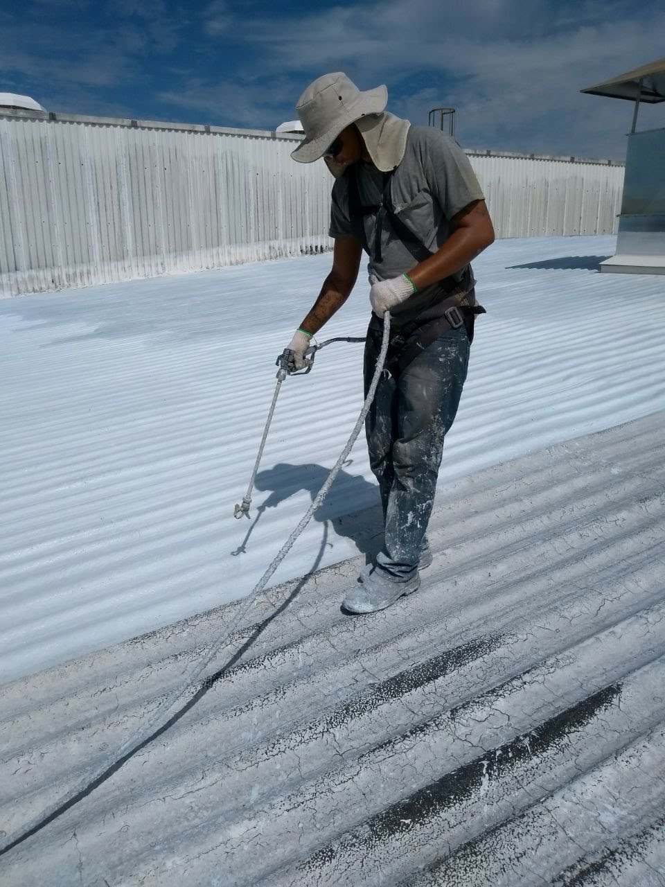 Telhado metálico corrugado industrial totalmente revestido com borracha líquida branca, vista ampla sob céu azul.