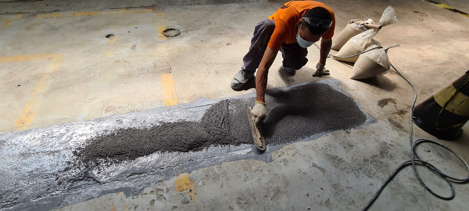 Aplicador espalhando massa estrutural em reparo localizado de piso industrial de concreto.
