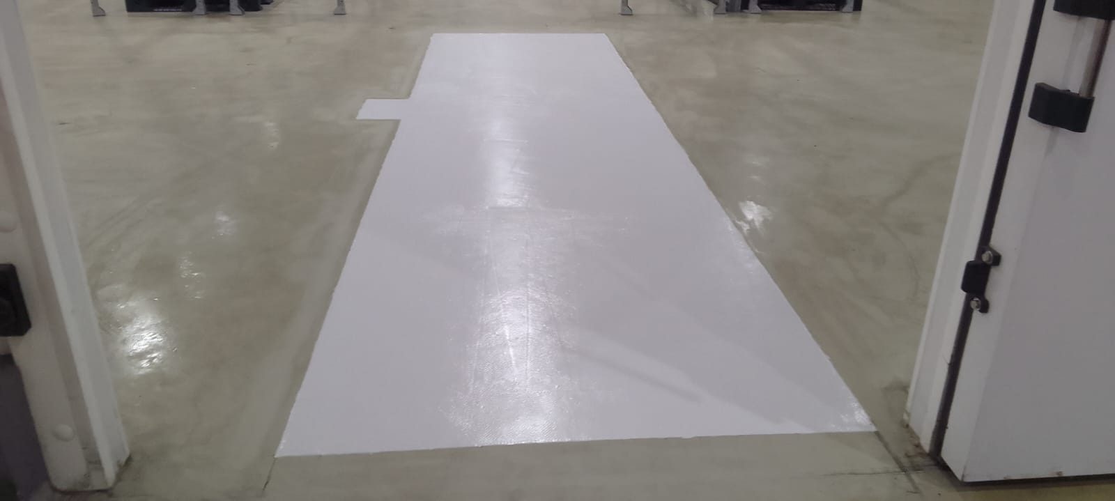 Reparo de piso industrial concluído entre portas de câmara fria, com acabamento claro e uniforme.