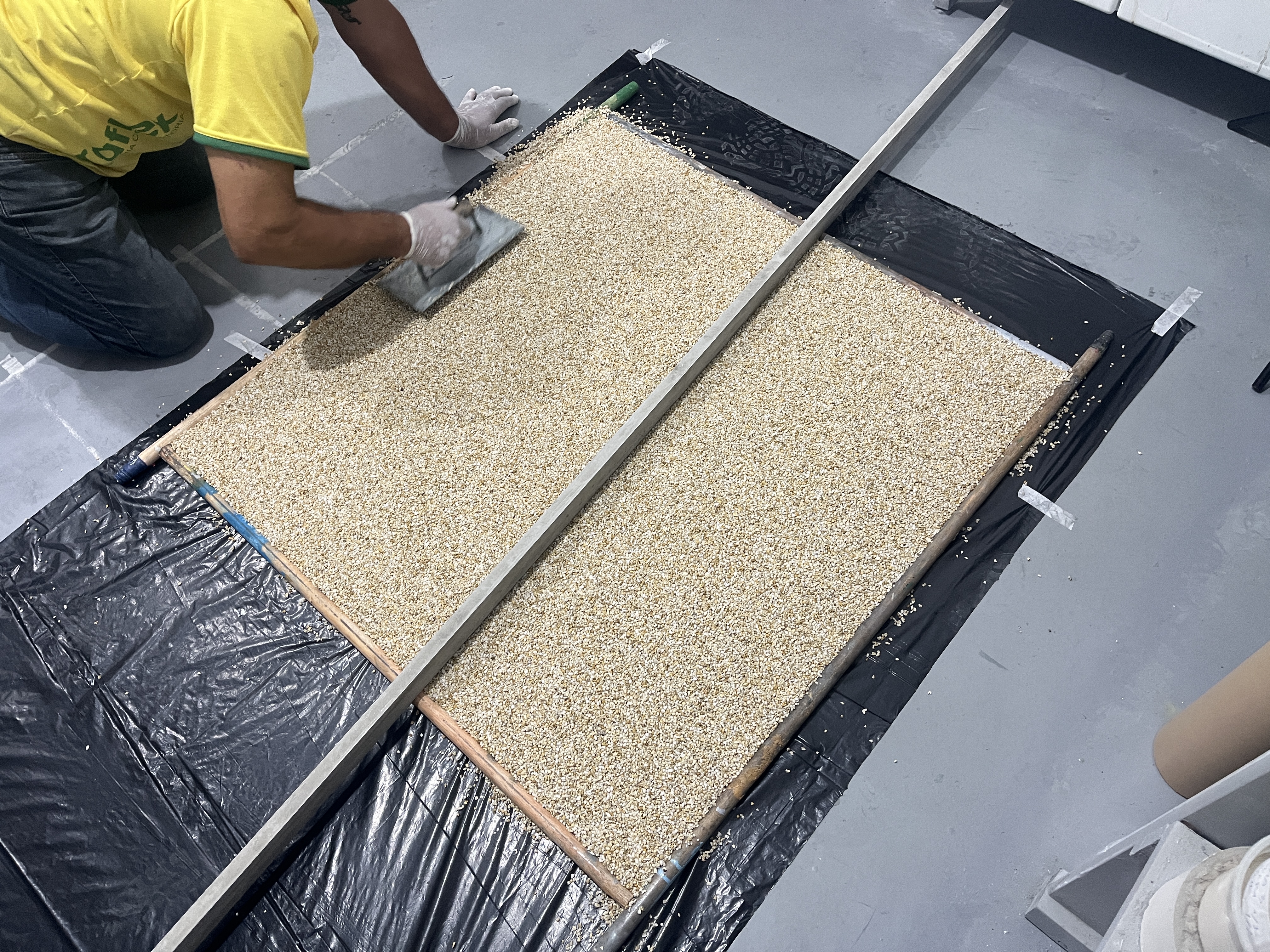 Aplicador nivelando grânulos de quartzo com desempenadeira sobre painel emoldurado, vista superior do processo de moldagem.