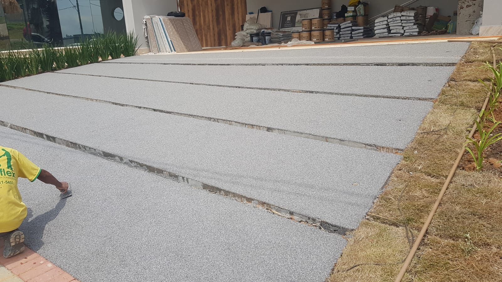 Rampa residencial finalizada com piso drenante cinza, aplicador Duraflex ajustando faixa de acabamento em primeiro plano.