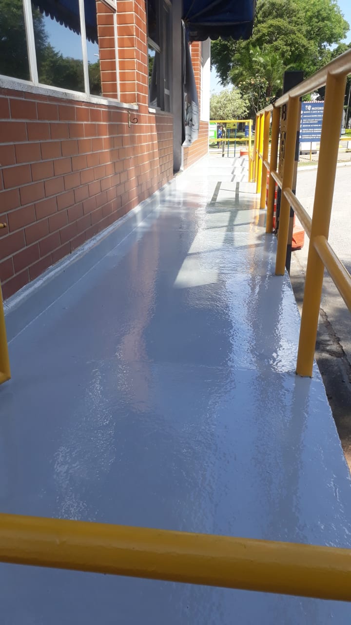 Piso em poliuretano azul-claro aplicado em passarela externa de prédio institucional, com corrimãos amarelos.