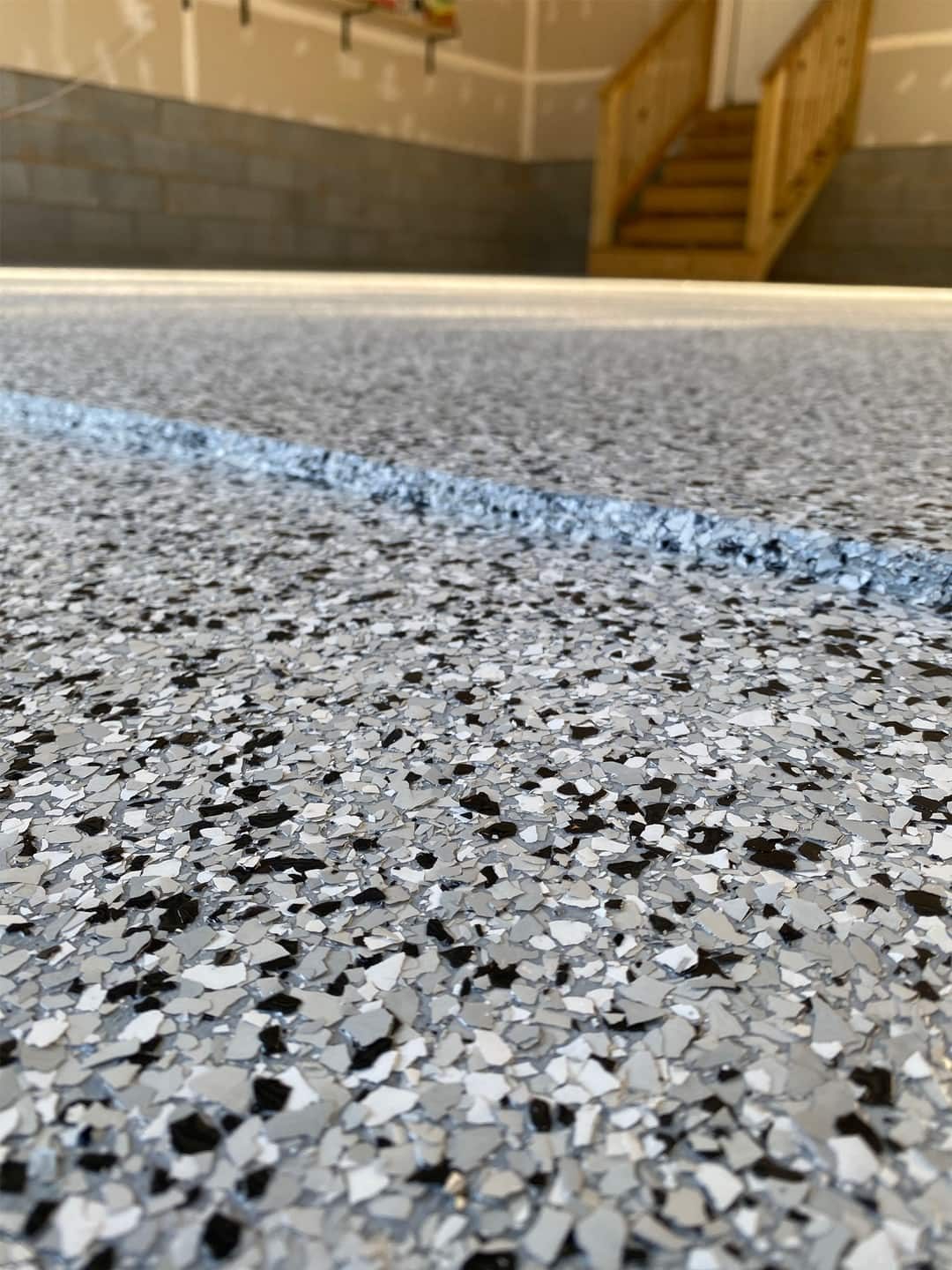 Close de piso epóxi flakes cinza e preto com faixa azul, mostrando a textura dos flocos de vinil.