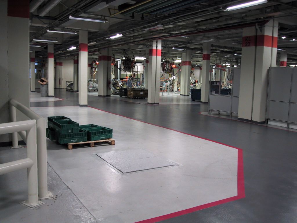 Piso epóxi espatulado cinza uniforme em corredor industrial, com painéis elétricos e estrutura metálica nas laterais.