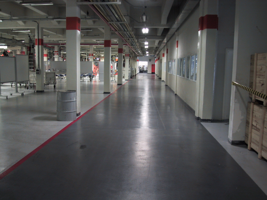 Piso epóxi espatulado cinza liso em fábrica automotiva, corredor amplo entre estações de trabalho.
