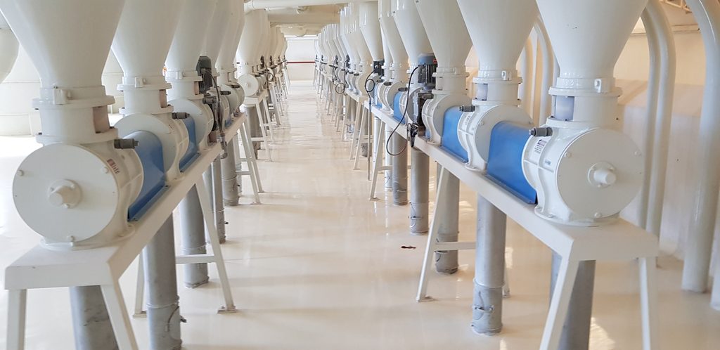 Corredor de indústria alimentícia com piso epóxi branco e equipamentos de moagem alinhados.