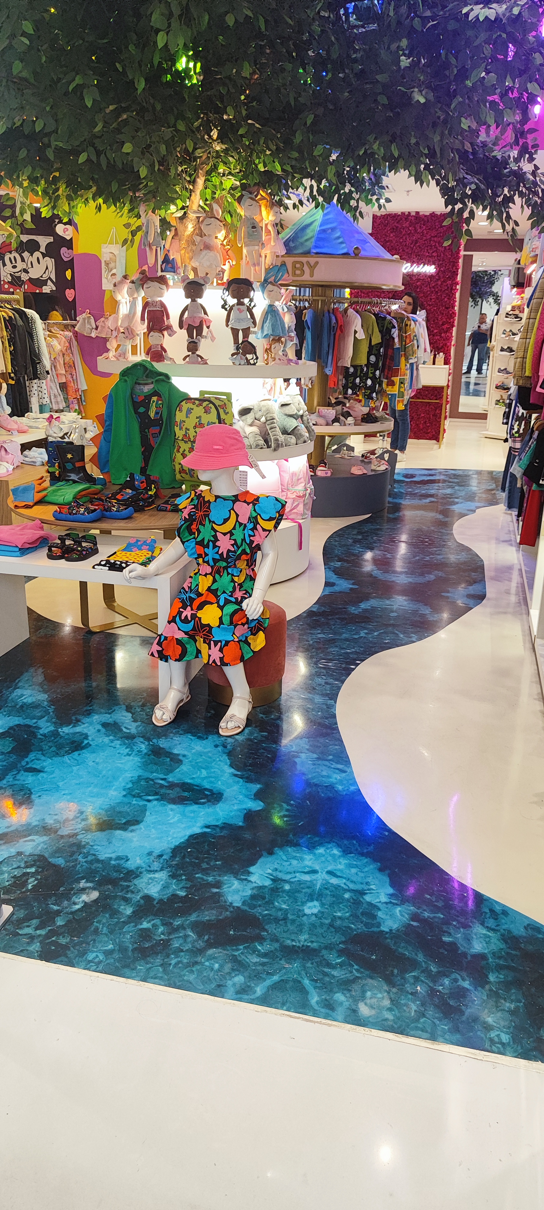 Corredor de loja infantil com piso epóxi azul marmorizado e áreas em branco, com manequim vestindo roupas coloridas.