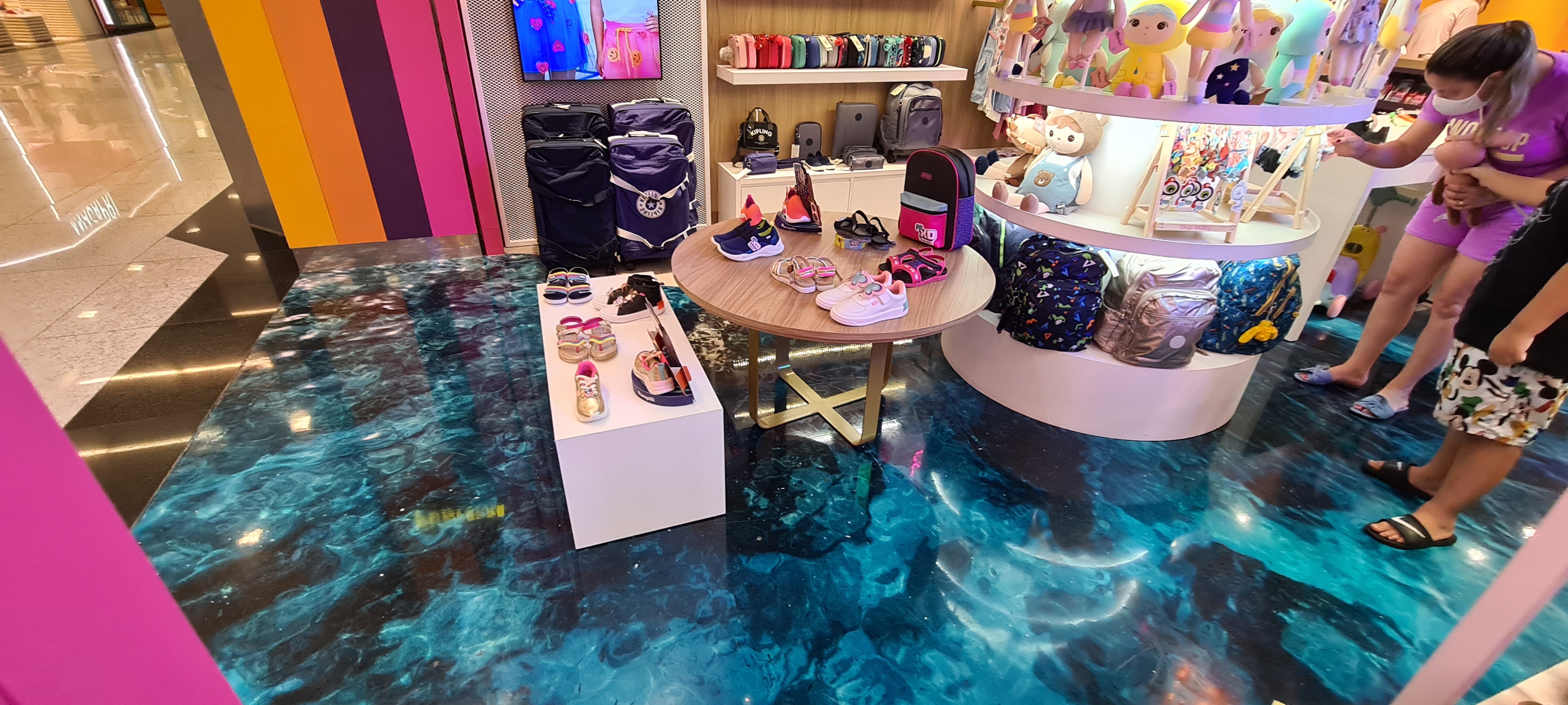 Piso epóxi com efeito oceano em tons de azul e turquesa em loja infantil, com produtos expostos sobre mesas e prateleiras.