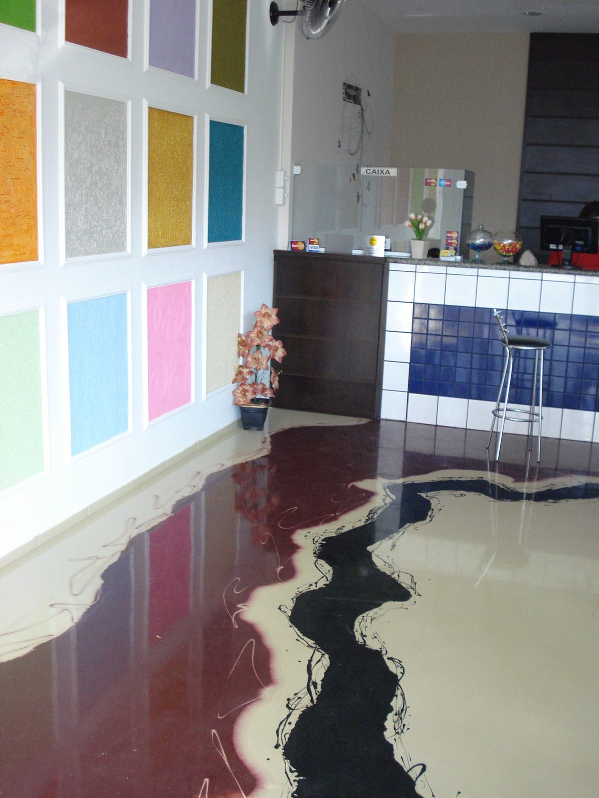 Piso epóxi 3D com efeito marmorizado em vermelho, preto e bege em cozinha com painel de vidros coloridos.