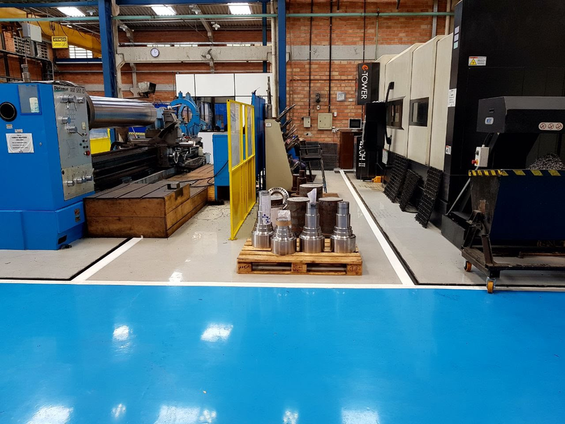 Setor de usinagem com piso epóxi autonivelante azul e torno mecânico ao fundo.