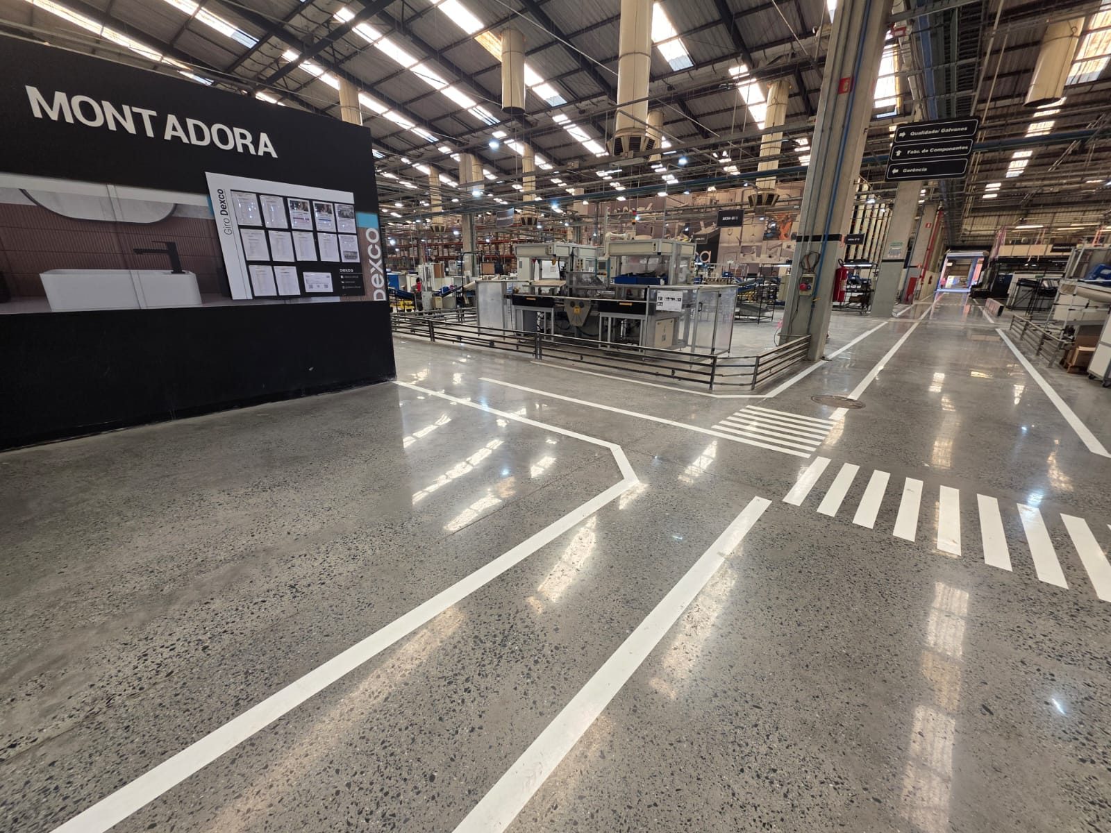 Piso de concreto polido em área de montagem industrial, com faixas brancas de circulação.