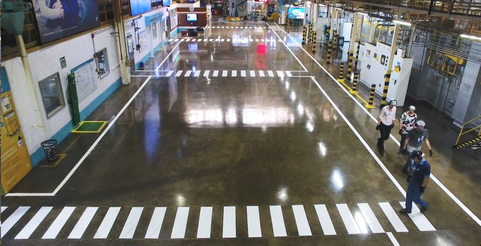 Piso de concreto polido em fábrica com faixa de demarcação, carrinhos de transporte e caixas ao fundo.
