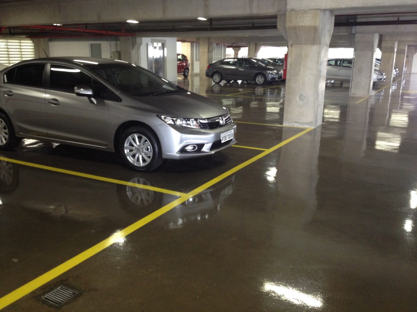 Garagem de condomínio com piso de concreto polido brilhante, demarcação amarela e veículos estacionados.
