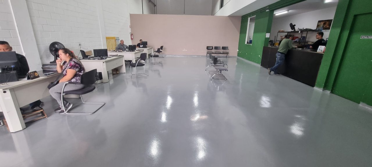 Escritório corporativo com piso epóxi cinza brilhante, estações de trabalho e parede verde ao fundo.