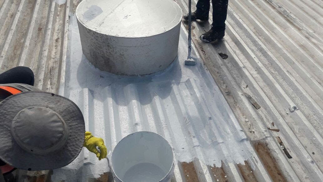 Aplicador impermeabilizando telhado de fibrocimento com tinta branca, com balde e recipiente de tinta ao lado.