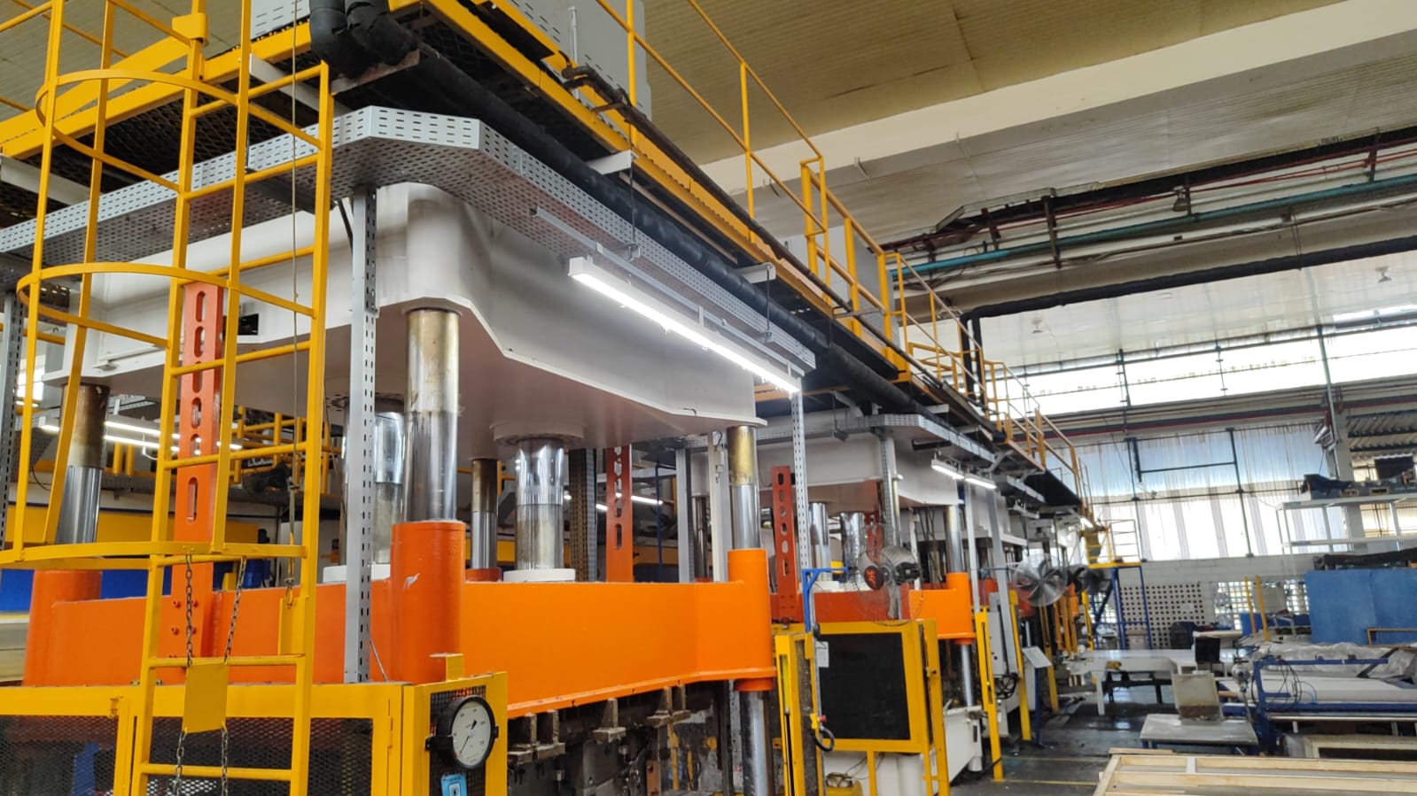 Prensa industrial de grande porte pintada em amarelo, laranja e branco, instalada em linha de produção fabril.